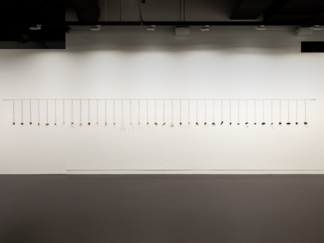 Areta Wilkinson’s ‘Ka taka te wa – Time passed 2022’ depicting a string with dangling pendants on a wall.